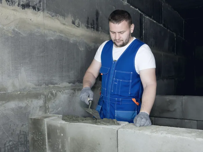 Maçon en gilet de travail qui monte un mur