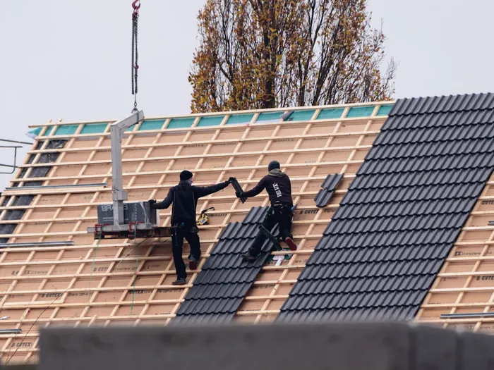 Couvreurs qui posent des tuiles sur une charpente neuve